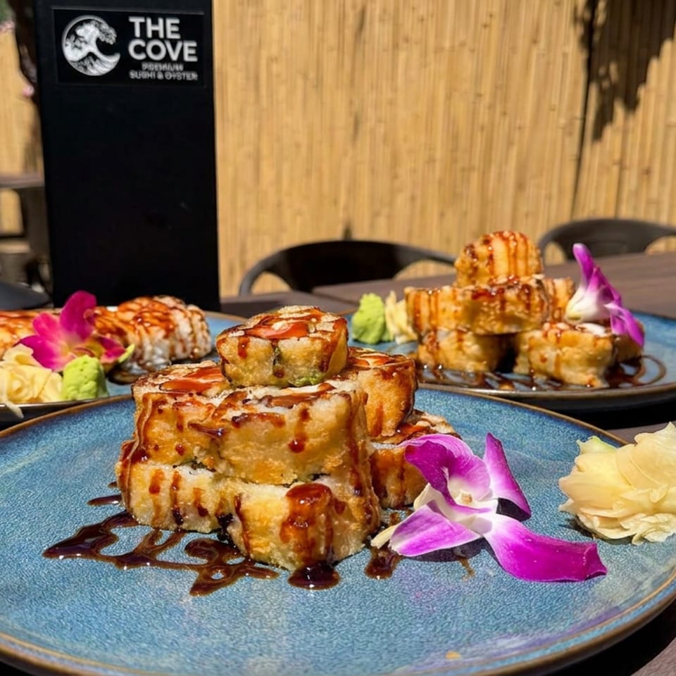 Sushi and golden-brown rolls drizzled with sauce, garnished with orchids, ginger, and wasabi on blue plates at The Cove.