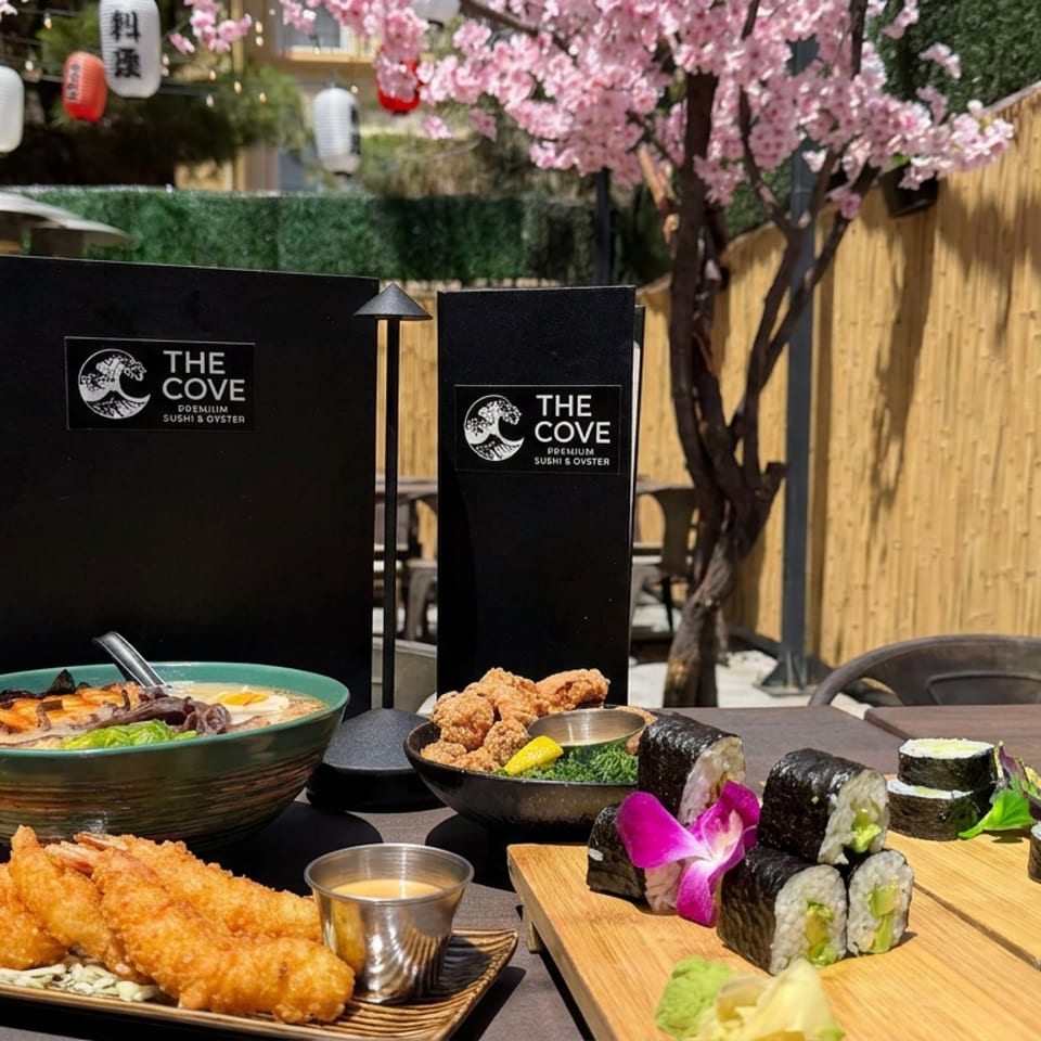 Sushi and Japanese dishes served on a restaurant patio with bamboo fencing, cherry blossoms, lanterns, and The Cove menus.